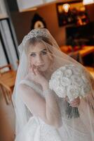 de bruid in een wit jurk, gedekt met een sluier, poses in mooi zo verlichting in haar kamer. ochtend- van de bruid. een mooi tiara foto