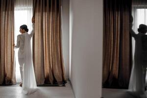 jong mooi bruid in wit pyjama in de ochtend. de bruid ochtend- Bij de hotel. lang modieus sluier. spiegel foto