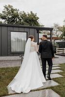 een wandelen van mooi bruiden Aan hun bruiloft dag in een geweldig plaats. tegen de achtergrond van een modern huis. foto van de terug