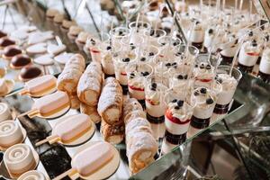 een heerlijk bruiloft. wit taart versierd met bloemen. snoep bar voor een banket. viering concept. modieus desserts. tafel met snoepgoed, snoepjes. fruit foto