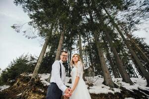 een jong stel, de bruid en bruidegom, glimlachend tonen uit hun bruiloft ringen tegen de achtergrond van hoog bomen. hebben een mooi zo tijd lachend. winter bruiloft foto