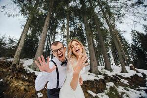 een jong stel, de bruid en bruidegom, glimlachend tonen uit hun bruiloft ringen tegen de achtergrond van hoog bomen. hebben een mooi zo tijd lachend. winter bruiloft foto