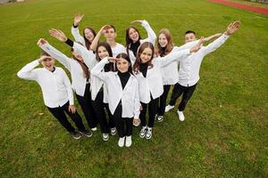 een groep van veel gelukkig tieners gekleed in de dezelfde kleding hebben pret en poseren in een stadion in de buurt een middelbare school. concept van vriendschap, momenten van geluk. school- vriendschap foto