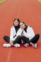 portret van twee tiener- meisjes in gewoontjes kleren zittend in een stadion en poseren op zoek Bij de camera. concept van vriendschap. een moment van geluk. foto