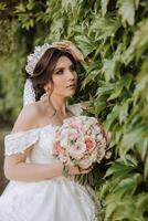 brunette bruid in off-the-schouder kant wit jurk en tiara poseren met een boeket van wit en roze bloemen. mooi haar- en verzinnen. voorjaar bruiloft foto