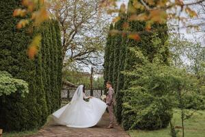 de bruid is cirkelen in haar bruiloft jurk, en de bruidegom is op zoek Bij haar. bruiloft foto sessie in een mooi voorjaar park.