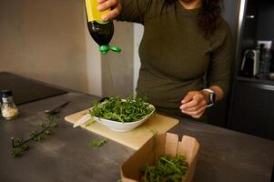 detailopname vrouw toevoegen olijf- olie in kom met vers groente salade Aan tafel in de huis keuken foto