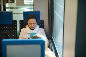 mooi vrouw forens genieten van haar comfortabel bedrijf reis, gebruik makend van mobiel telefoon terwijl op reis door trein. foto