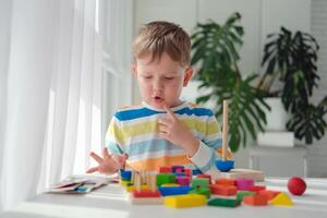 een weinig jongen Toneelstukken met houten speelgoed en bouwt een toren. leerzaam logica speelgoed voor kinderen. montessori spellen voor kind ontwikkeling. kinderen houten speelgoed. foto