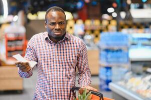 verrast Afro-Amerikaans Mens looks Bij bon totaal in verkoop controleren Holding papier zak foto