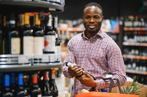 Afrikaanse Amerikaans Mens Holding fles van wijn en op zoek Bij het terwijl staand in een wijn op te slaan foto