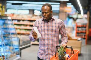 verrast Afro-Amerikaans Mens looks Bij bon totaal in verkoop controleren Holding papier zak foto