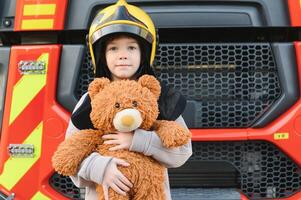 een jongen vervelend een brandweerman helm in de buurt een brand vrachtwagen. foto