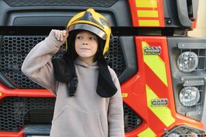 kind, schattig jongen, gekleed in brand vechters doeken in een brand station met brand vrachtwagen, kinderen droom foto