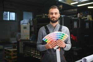 het drukken huis interieur met modern offset afdrukken machine en operator in werken uniform controle kwaliteit en controlerend werkwijze van afdrukken foto