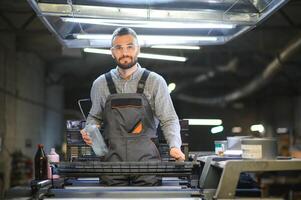 het drukken huis interieur met modern offset afdrukken machine en operator in werken uniform controle kwaliteit en controlerend werkwijze van afdrukken foto