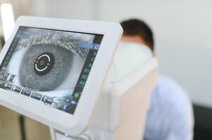 knap jong Mens is controle de oog visie in modern oogheelkunde kliniek. geduldig in oogheelkunde kliniek foto