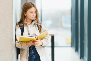 portret van glimlachen schoolmeisje staand met notitieboekje in gang Bij school- foto