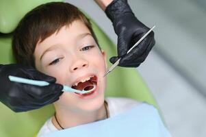 schattig jongen glimlachen terwijl tanden tentamen . gelukkig jongen zittend in tandartsen stoel en hebben controleren omhoog tanden foto