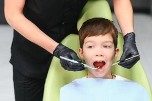 schattig jongen glimlachen terwijl tanden tentamen . gelukkig jongen zittend in tandartsen stoel en hebben controleren omhoog tanden foto