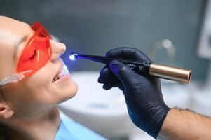 jong vrouw krijgen tandheelkundig vulling drogen procedure met genezen uv licht Bij tandheelkundig kliniek foto