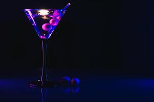 glas van klassiek droog martini cocktail met olijven Aan donker tafel tegen zwart achtergrond. met vrij ruimte voor uw tekst foto