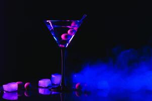 martini glas en olijven Aan een zwart achtergrond met neon lichten foto