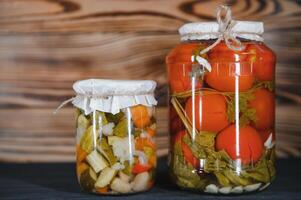 glas potten met gepekeld komkommers augurken, gepekeld tomaten en kool. potten van divers gepekeld groenten. ingeblikt voedsel in een rustiek samenstelling. foto