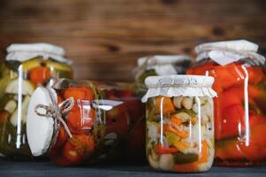 glas potten met gepekeld komkommers augurken, gepekeld tomaten en kool. potten van divers gepekeld groenten. ingeblikt voedsel in een rustiek samenstelling. foto