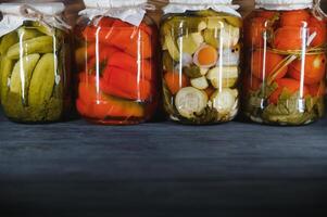 glas potten met gepekeld komkommers augurken, gepekeld tomaten en kool. potten van divers gepekeld groenten. ingeblikt voedsel in een rustiek samenstelling. foto