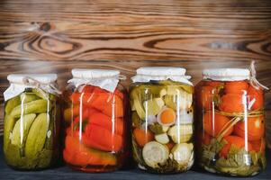 glas potten met gepekeld komkommers augurken, gepekeld tomaten en kool. potten van divers gepekeld groenten. ingeblikt voedsel in een rustiek samenstelling. foto