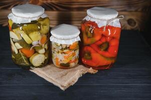 glas potten met gepekeld komkommers augurken, gepekeld tomaten en kool. potten van divers gepekeld groenten. ingeblikt voedsel in een rustiek samenstelling. foto