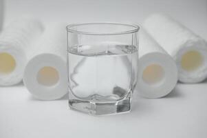 een glas van drinken water en filter inktpatronen Bij wit achtergrond foto