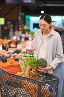 jong vrouw kiest broccoli, buying groenten in supermarkt. foto