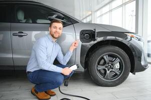 baard Mens proberen een nieuw opladen kabel met een auto opladen station Bij de motor dealerschap. concept van buying elektrisch voertuig. slim ecologisch leven foto