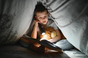 jongen met zaklamp lezing boek onder deken Bij huis foto