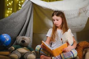 gelukkig kind meisje lachend en lezing boek in donker in een tent Bij huis. foto