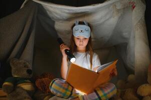 weinig meisje zijn lezing een boek met zaklampen in tent. gelukkig meisje spelen Bij huis. grappig lief kind hebben pret in kamer foto