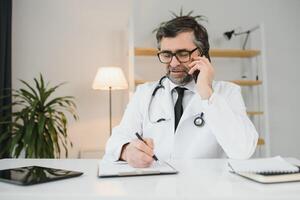 portret van een professioneel vriendelijk senior dokter gebruik makend van een mobiel telefoon. foto