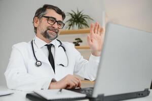 afgelegen medisch overleg. een mannetje dokter overlegt een vrouw heeft een video telefoontje conferentie computer toezicht houden op zittend in een kliniek kantoor foto