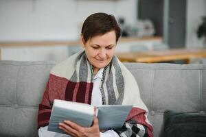 portret van senior vrouw Bij huis Aan sofa met plaid foto