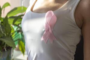 schot van de vrouw tegen de wit muur in de wit top met roze lint, net zo een symbool van een borst kanker bewustzijn. concept foto