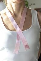 schot van de vrouw in de wit top tegen de wit muur, met roze lint Aan haar nek net zo een symbool van borst kanker bewustzijn. concept foto