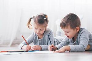 kinderen liggen in pyjama op de grond en tekenen met potloden. schattig kind schilderen met potloden foto