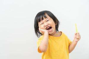 weinig Aziatisch meisje persen hand- naar wang, lijdt van pijn in tand. tanden verval, tandheelkundig problemen, kind emoties en gelaats uitdrukking, mondeling Gezondheid zorg, verminderen snoepgoed, fluor coating foto