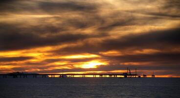 een zonsondergang over- de zee met pier in silhouet foto