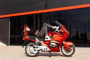 een vrouw poses sierlijk Aan een levendig rood motorfiets. een vrouw houdende Aan top van een rood motorfiets foto