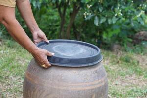 detailopname handen houden deksel naar Hoes water pot naar beschermen van muggen naar ras binnen of andere insecten of stof Gaan in water. concept, campagne naar hou op muggen fiets naar leggen eieren in water houder foto