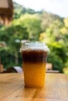 verkoudheid zwart koffie met vers oranje sap, het tonen de structuur van twee laag en verfrissend kijken van de drinken Aan hout tafel. foto