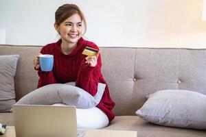 een jong Aziatisch vrouw met een gelukkig glimlach houdt een credit kaart en toepassingen een smartphone naar winkel online online betaling concept. foto